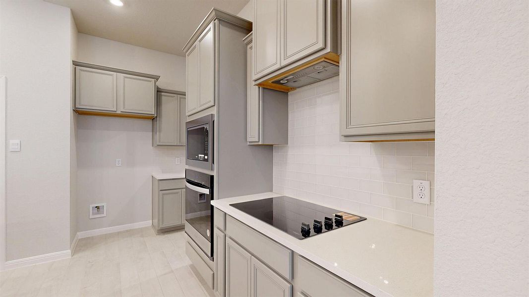 Kitchen featuring gray cabinets, stainless steel appliances, decorative backsplash, light wood-type flooring, and light stone countertops Kitchen featuring gray cabinets, stainless steel appliances, decorative backsplash, light wood-type flooring, and light stone countertops