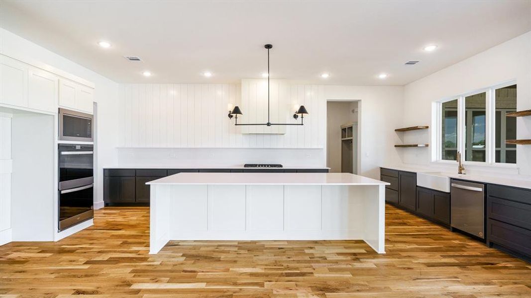 Kitchen featuring light hardwood / wood-style floors, pendant lighting, a kitchen island, white cabinetry, and appliances with stainless steel finishes