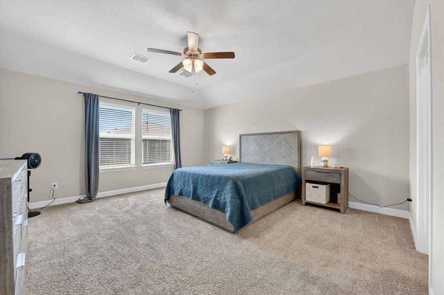 Spacious bedroom featuring light-toned carpeting, a ceiling fan with integrated lighting, and multiple windows providing ample natural light