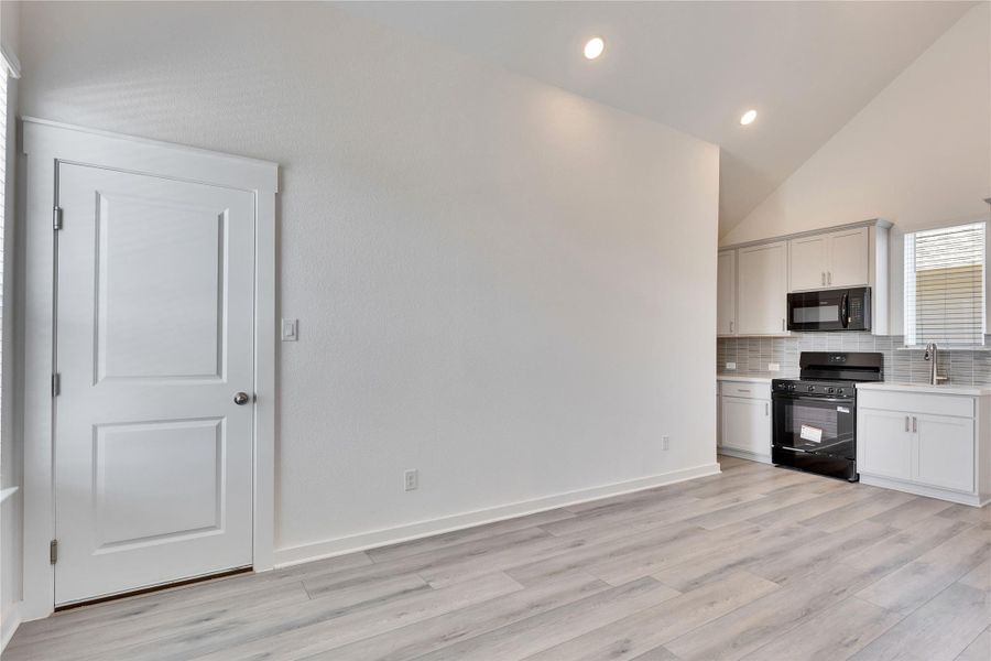Kitchen featuring black appliances, tasteful backsplash, light wood-type flooring, recessed lighting, and high vaulted ceiling