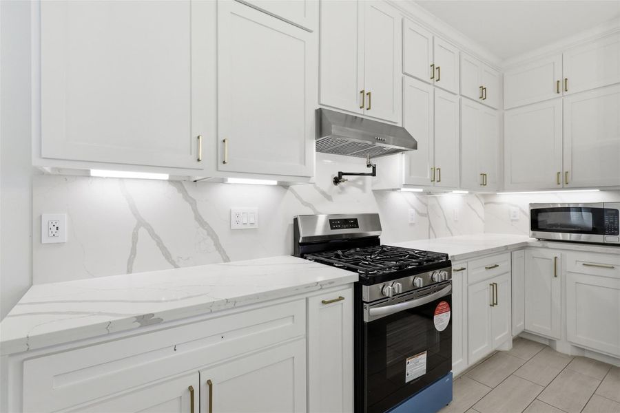 Kitchen featuring white cabinetry, quartz countertops, stainless steel gas range, and subway tile backsplash.