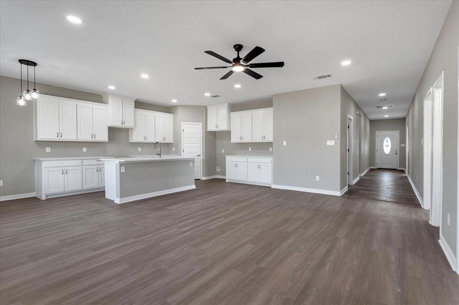 Kitchen featuring a center island with sink, light countertops, dark wood finished floors, white cabinets, and recessed lighting