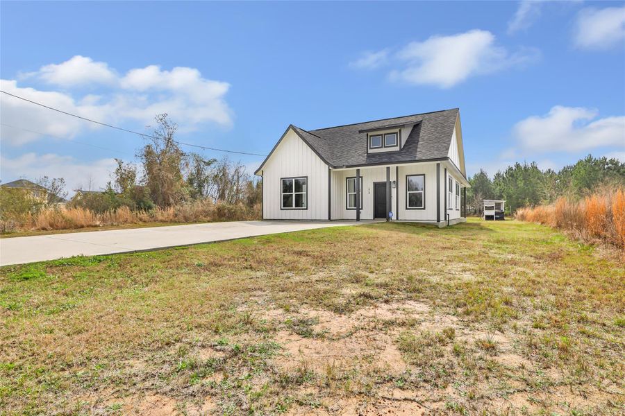 Modern, single-story home with a gabled roof and large windows, set on a spacious lot with a concrete driveway and grassy surroundings, offering a serene and private setting.