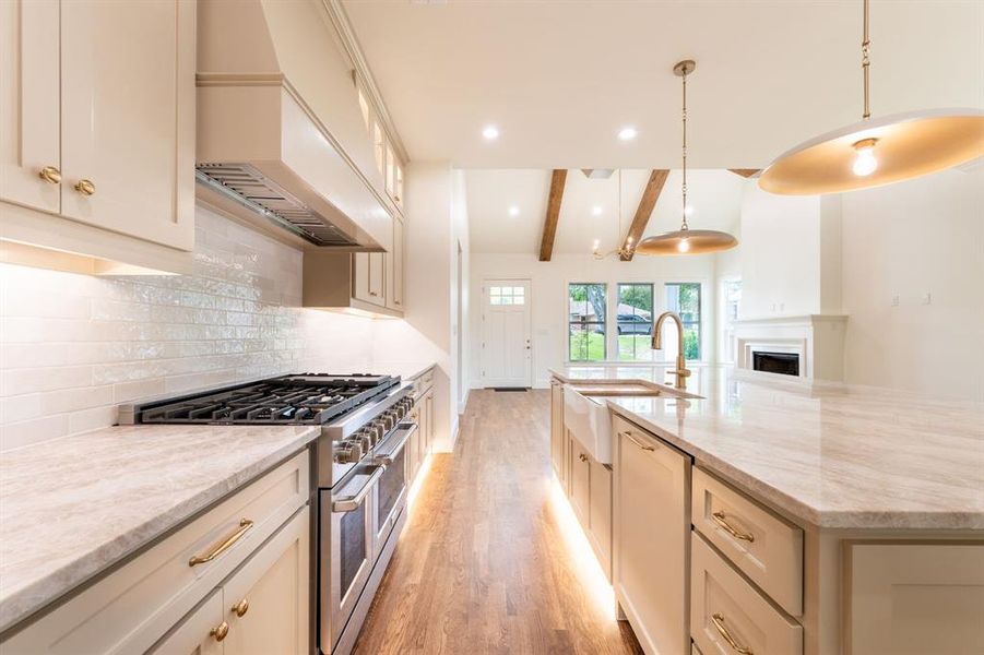 Gourmet kitchen featuring a professional-grade gas range, built-in hood, under-cabinet lighting, a farmhouse sink, and polished countertops Gourmet kitchen featuring a professional-grade gas range, built-in hood, under-cabinet lighting, a farmhouse sink, and polished countertops