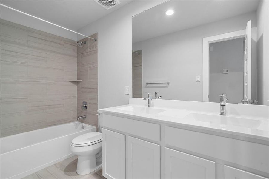 Secondary bath features tile flooring, bath/shower combo with tile surround, stained cabinets, beautiful light countertops, mirror, sleek fixtures and modern finishes.