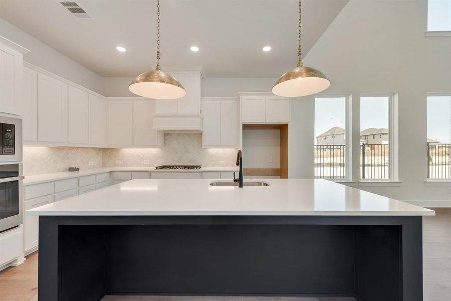 Kitchen with decorative backsplash, white cabinets, light wood-type flooring, an island with sink, and hanging light fixtures Kitchen with decorative backsplash, white cabinets, light wood-type flooring, an island with sink, and hanging light fixtures