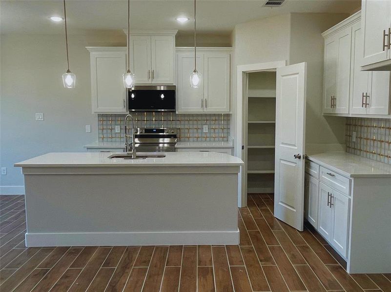 Kitchen featuring a kitchen island with sink, sink, decorative light fixtures, and white cabinets