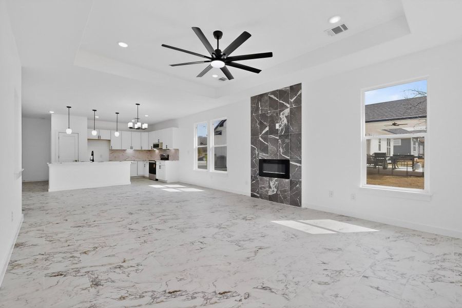Unfurnished living room featuring a fireplace, a tray ceiling, ceiling fan, suspended lighting,