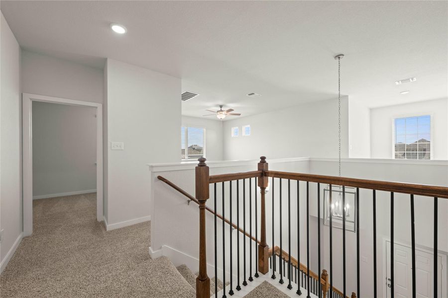A well-lit upstairs landing features carpeted flooring and a sturdy wood and iron railing, overlooking the entrance below.