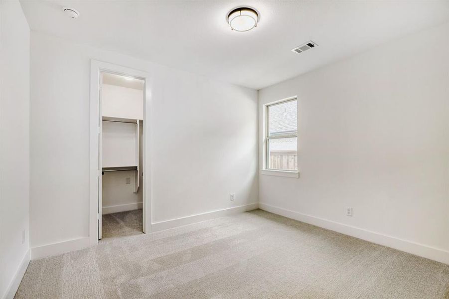 Unfurnished bedroom featuring light colored carpet and a walk in closet