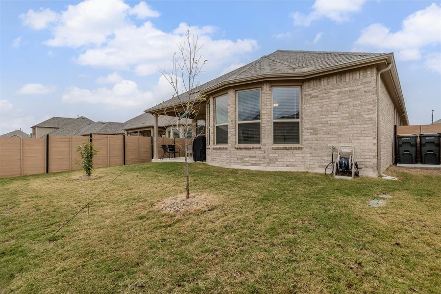 Rear view of house with brick siding, a fenced backyard, a patio area, and a shingled roof