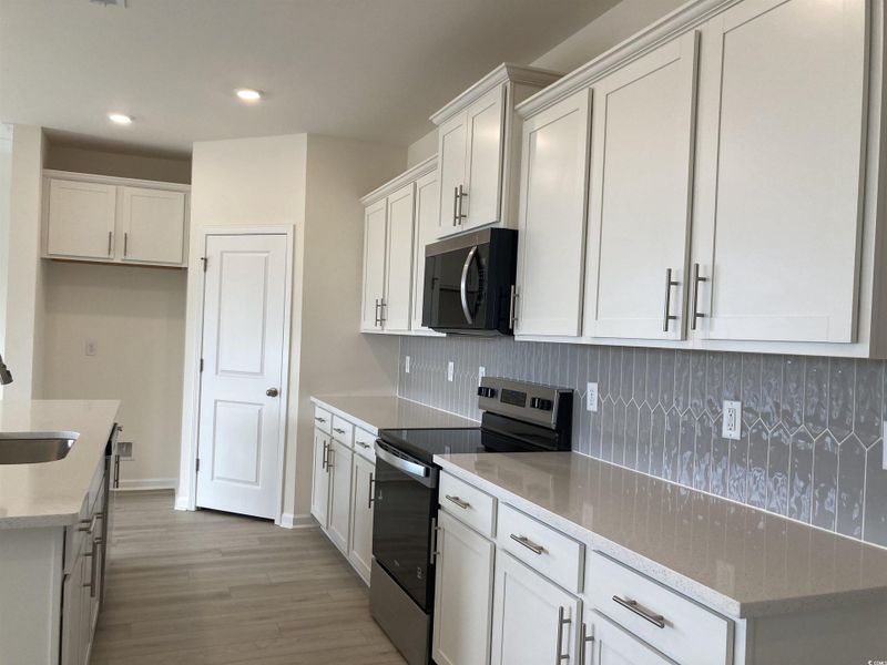 Kitchen featuring stainless steel appliances, light stone countertops, white cabinets, light wood finished floors, and decorative backsplash