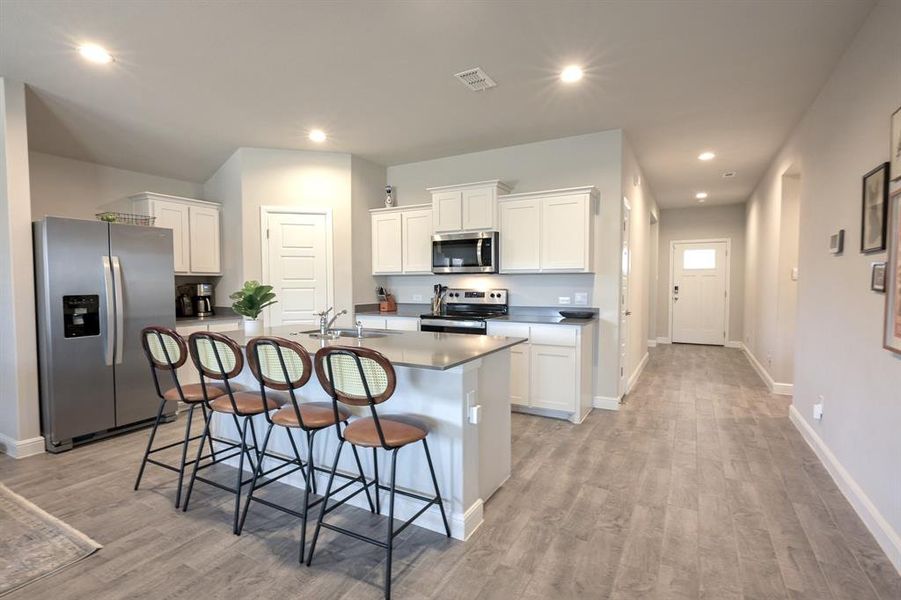 Kitchen with tile wood -look floors, appliances with stainless steel finishes, white cabinets, a sink, and an island with sink