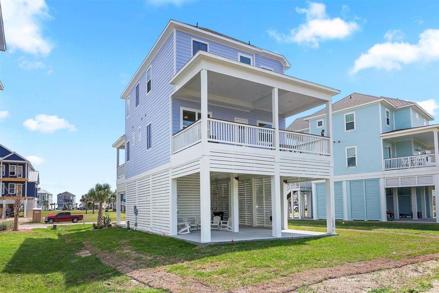 This rear view of the home highlights multiple balconies, covered patio space, and a spacious yard—all just a short walk to the beach crossover.
