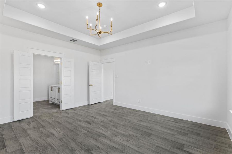 Unfurnished Master bedroom with a tray ceiling, ensuite bath, dark hardwood / wood-style flooring, and a chandelier