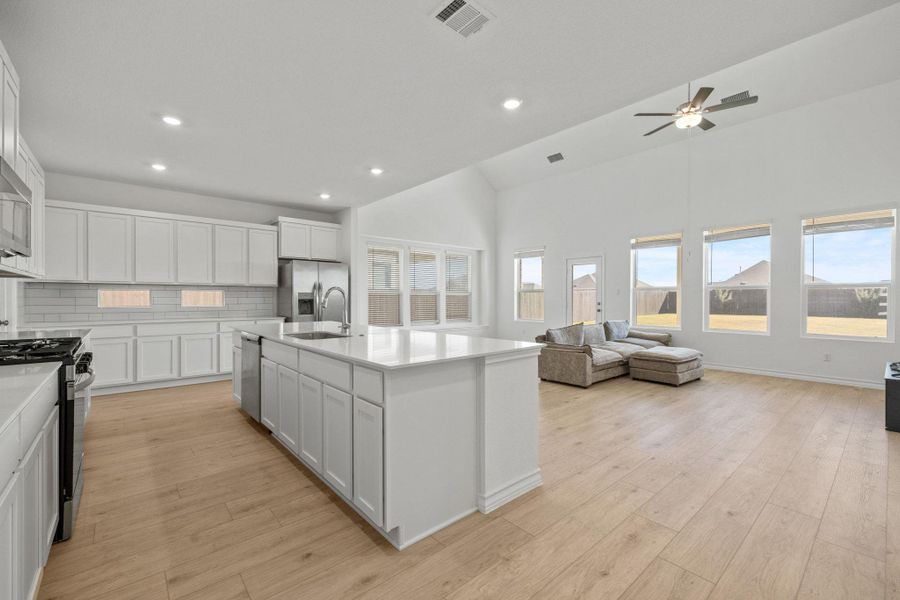 Kitchen with white cabinetry, tasteful backsplash, stainless steel appliances, light wood-type flooring, and a kitchen island with sink