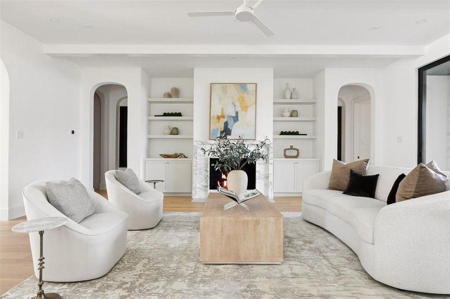 Living room featuring arched walkways, a fireplace, light wood-style flooring, ceiling fan, and beam ceiling Living room featuring arched walkways, a fireplace, light wood-style flooring, ceiling fan, and beam ceiling