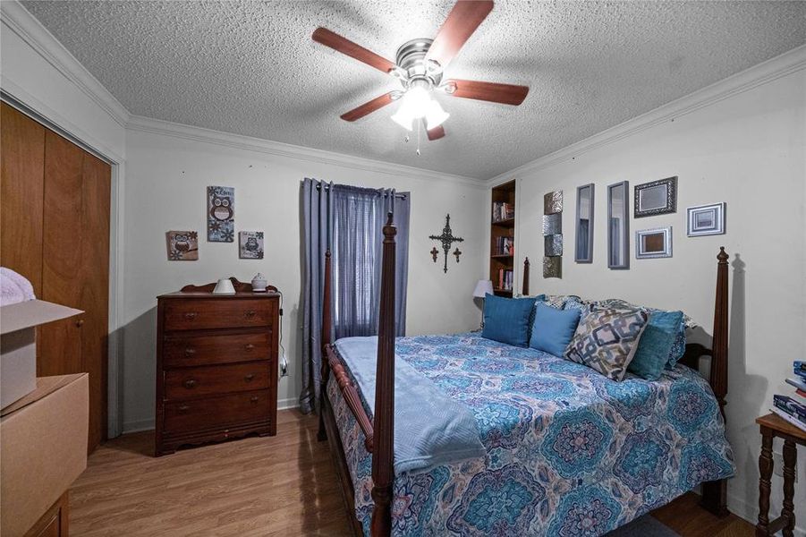Bedroom featuring a textured ceiling, wood finished floors, crown molding, and a ceiling fan