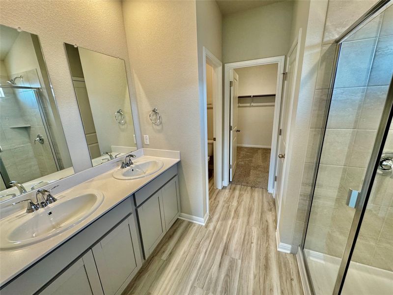 Bathroom with a stall shower, double vanity, a walk in closet, light wood-style flooring, and a textured wall Bathroom with a stall shower, double vanity, a walk in closet, light wood-style flooring, and a textured wall