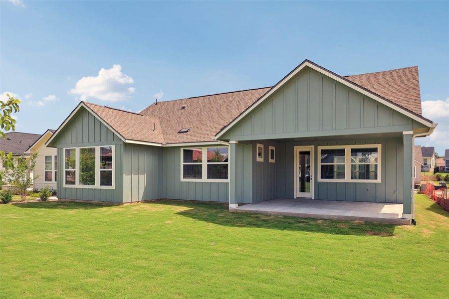 Rear view of property featuring roof with shingles, board and batten siding, a patio, and a lawn
