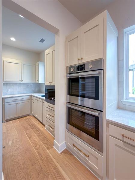 Kitchen featuring light wood-finish flooring, white cabinetry with brass hardware, a built-in double oven, and recessed lighting