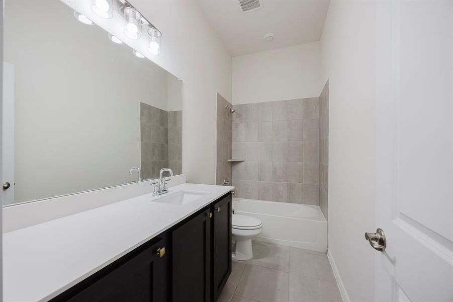 Full bathroom with tile patterned floors, toilet, vanity, and tiled shower / bath combo