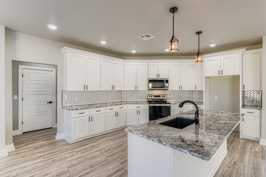 Kitchen with stainless steel appliances, tasteful backsplash, hanging light fixtures, white cabinets, and light stone counters