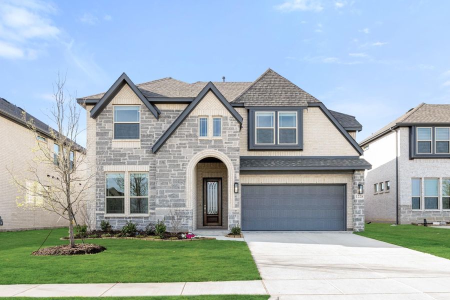 Two-story home with stone exterior, arched entry, two-car garage, and green front lawn Two-story home with stone exterior, arched entry, two-car garage, and green front lawn