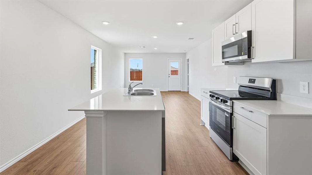 Kitchen featuring stainless steel appliances, a kitchen island with sink, white cabinets, light wood-style flooring, and recessed lighting