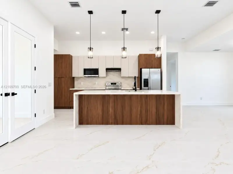 Contemporary kitchen featuring a dual-tone cabinetry design, quartz waterfall island, large-format tile flooring, and three pendant lights