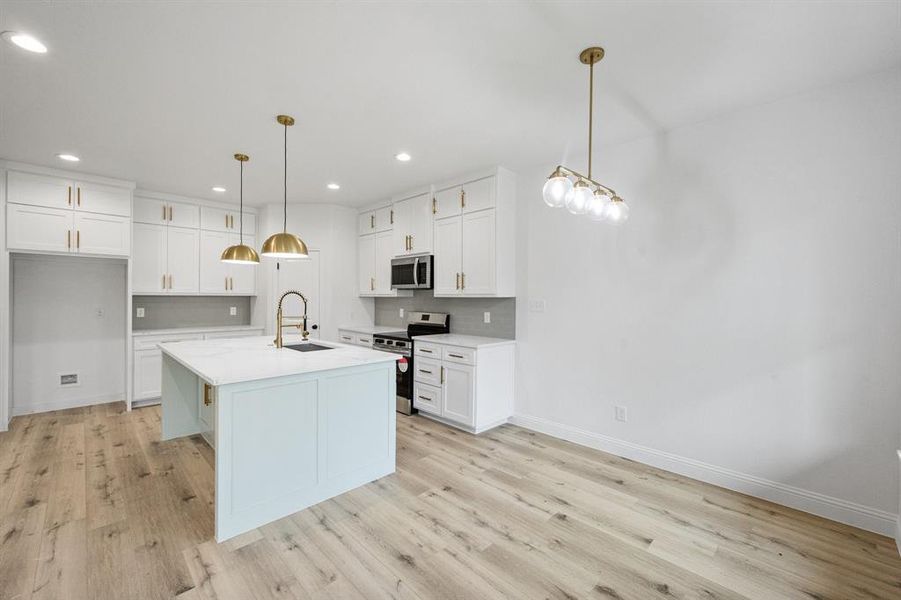 Kitchen with stainless steel appliances, white cabinets, light countertops, and a sink