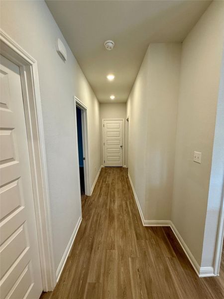 Hallway featuring wood-finish flooring, white baseboards, recessed ceiling lighting, and a paneled interior door