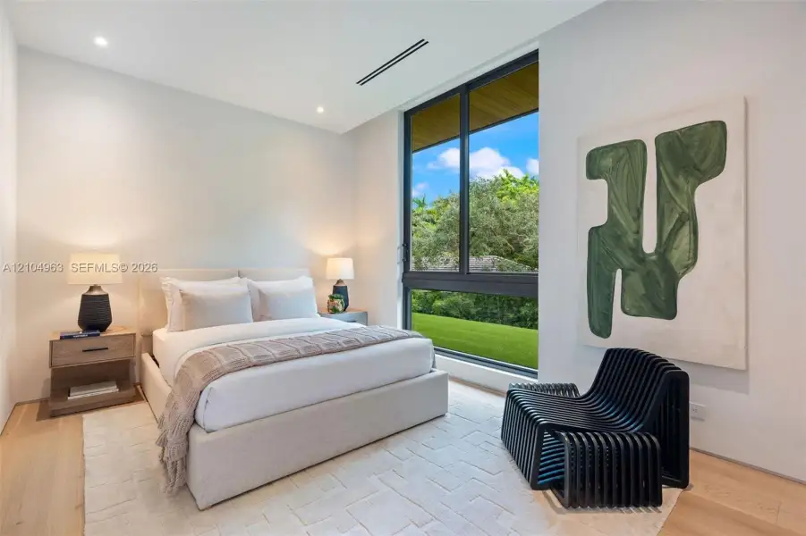 Modern bedroom featuring wood-finish flooring, recessed lighting, and a large, fixed-pane window with a black frame