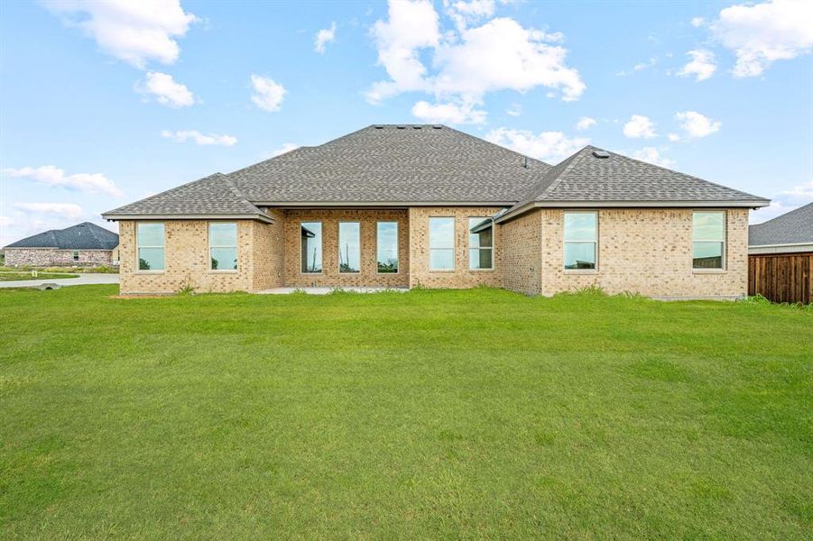 Rear view of house with a lawn, roof with shingles, brick siding, and a patio area