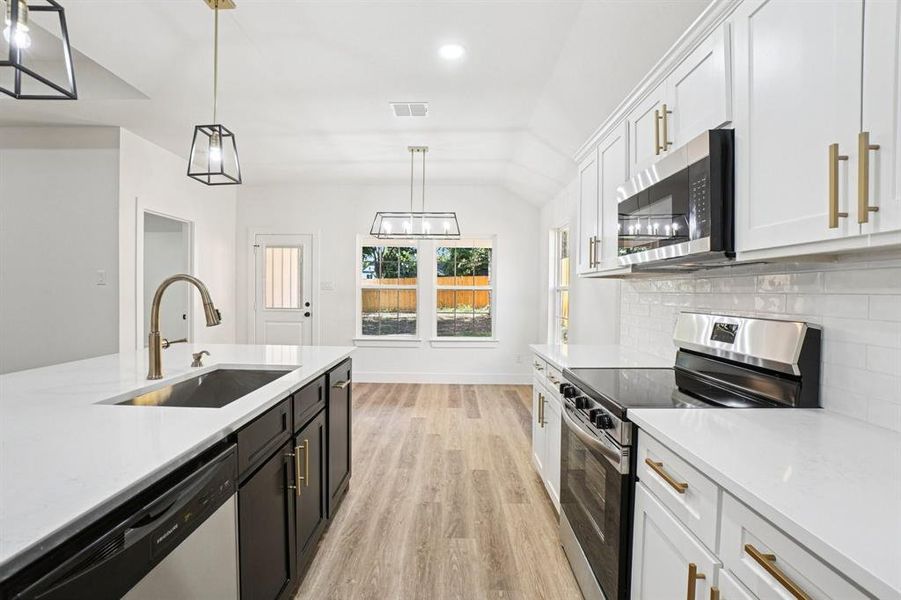 Kitchen featuring white cabinets, appliances with stainless steel finishes, hanging light fixtures, light stone counters, and vaulted ceiling Kitchen featuring white cabinets, appliances with stainless steel finishes, hanging light fixtures, light stone counters, and vaulted ceiling
