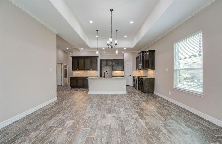 This is a spacious, modern open-concept kitchen and living area featuring wood-look tile flooring, dark wood cabinetry, a large center island, recessed lighting, and ample natural light from the window.