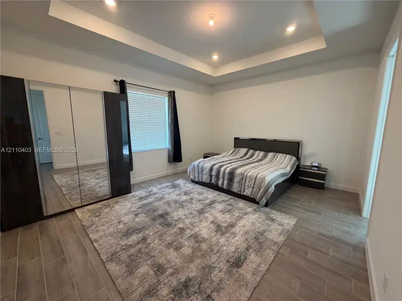 Tray ceiling with recessed lighting, wood-finish tile flooring, and integrated full-length mirrored wardrobe