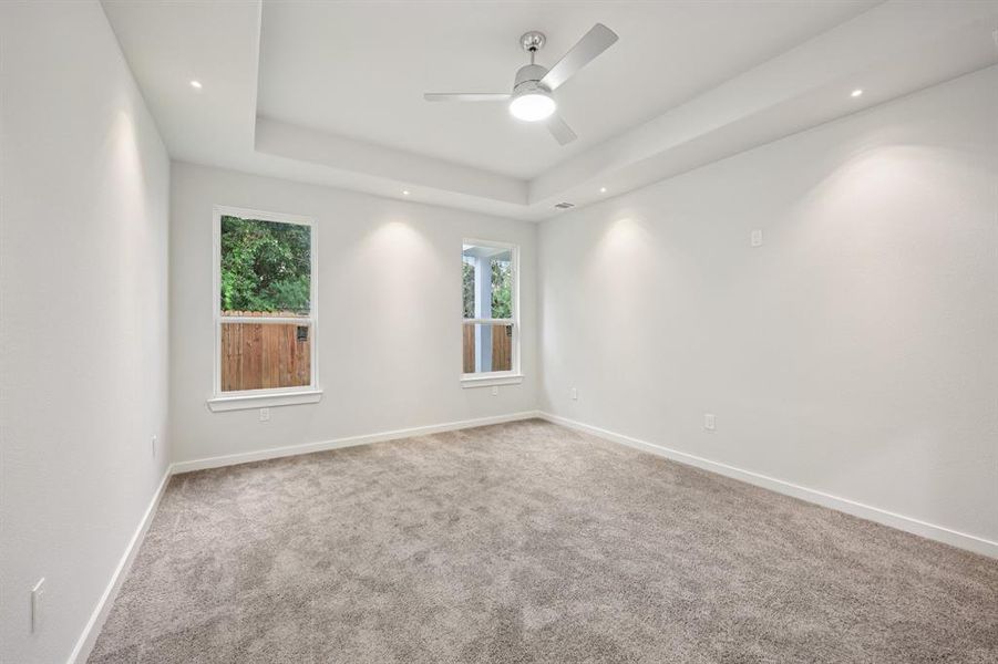 Carpeted empty room with plenty of natural light, ceiling fan, a raised ceiling, and recessed lighting Carpeted empty room with plenty of natural light, ceiling fan, a raised ceiling, and recessed lighting