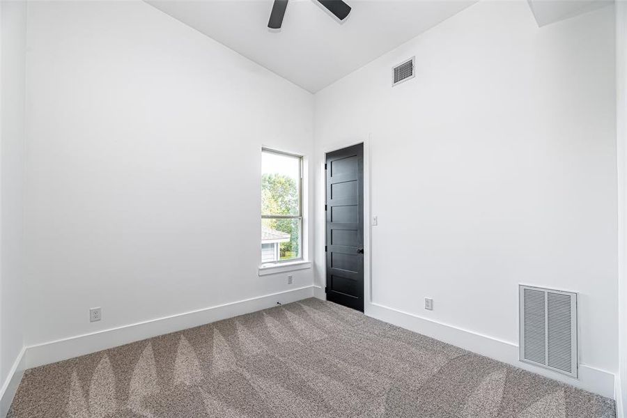 This is a bright and clean room featuring a neutral color scheme with fresh white walls and plush carpeting. It includes a window for natural light and a modern black door, suggesting a contemporary design.