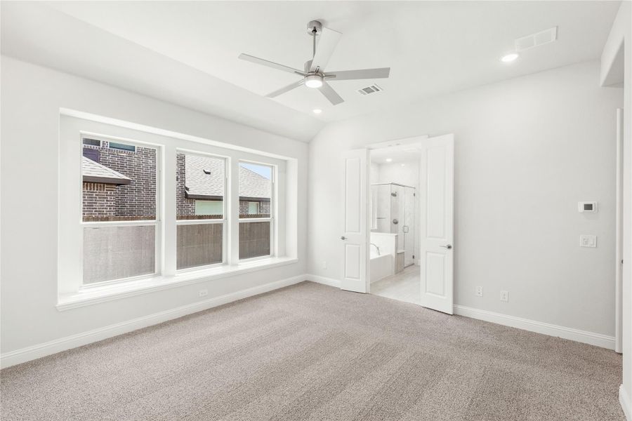 Empty bedroom with carpet, ceiling fan, vaulted ceiling, and open ensuite bathroom door