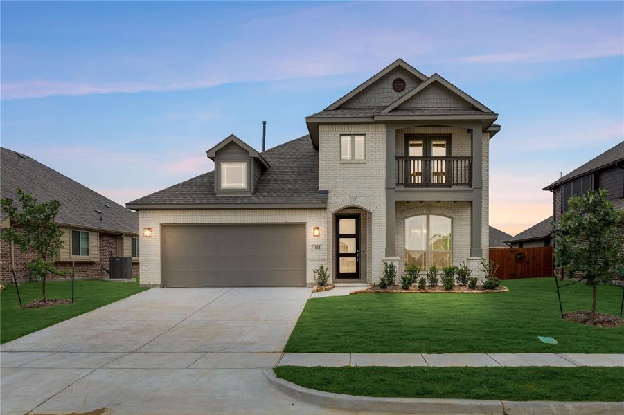 Two-story home with white brick exterior, two-car garage, and upper balcony with green front lawn Two-story home with white brick exterior, two-car garage, and upper balcony with green front lawn
