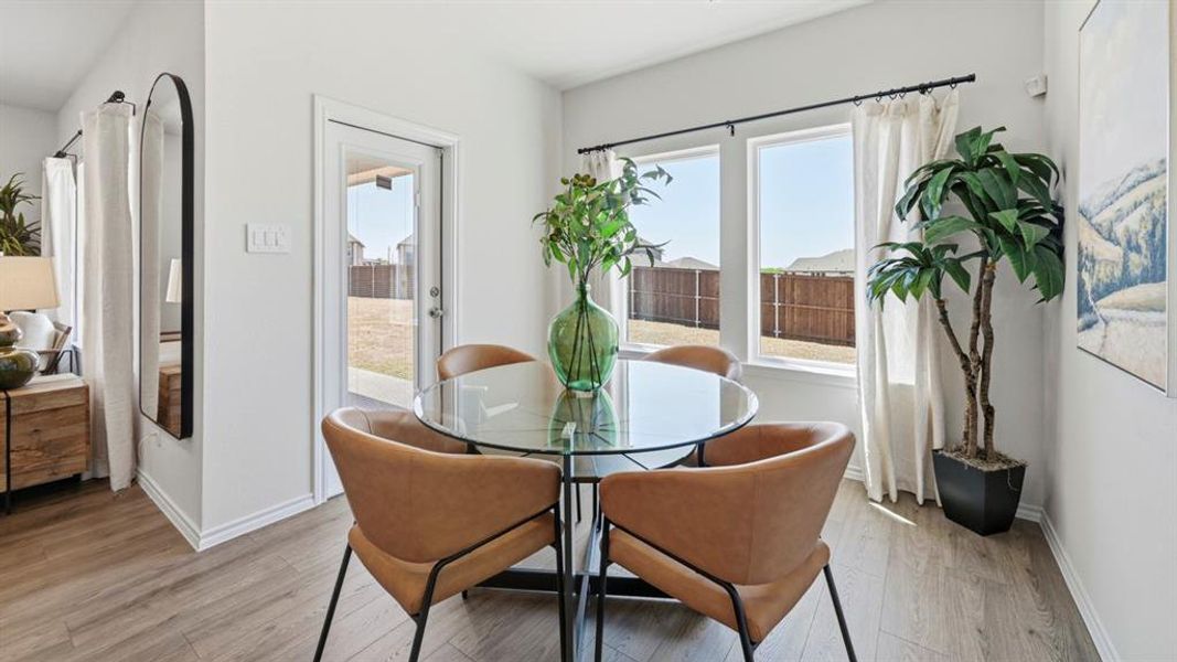 Dining area with wood-finish flooring, featuring a glass-top table, white walls, and multiple windows Dining area with wood-finish flooring, featuring a glass-top table, white walls, and multiple windows