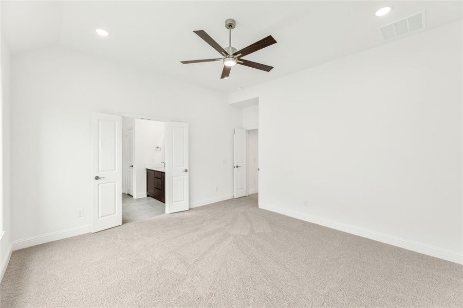 Empty bedroom with carpet, ceiling fan, and open doors leading to an ensuite bathroom Empty bedroom with carpet, ceiling fan, and open doors leading to an ensuite bathroom