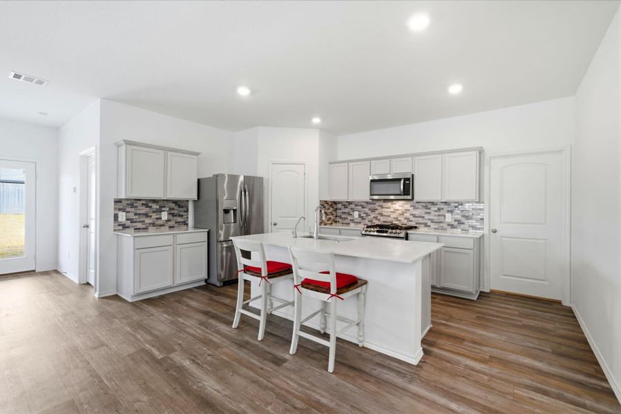Gourmet-ready kitchen with modern quartz countertops, shaker cabinetry, neutral backsplash, and durable vinyl plank flooring. SS appliances complete the look.