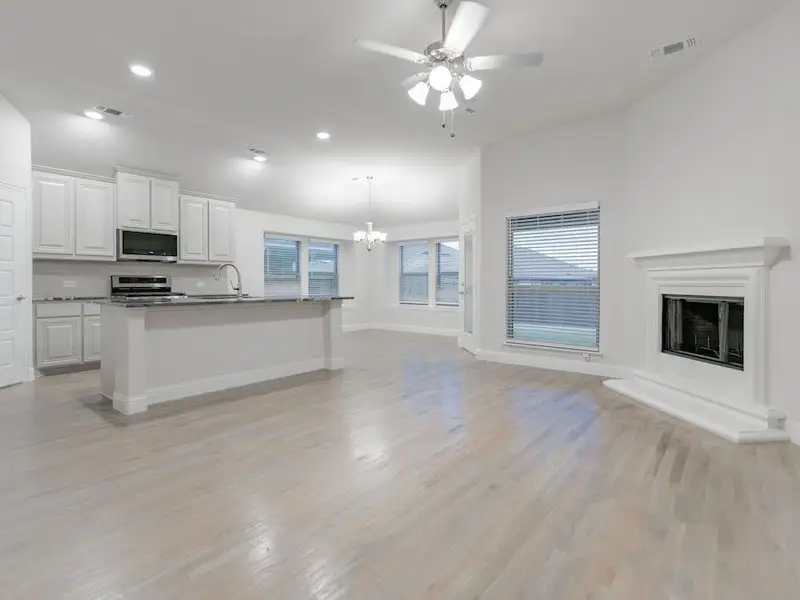 Kitchen featuring ceiling fan with notable chandelier, stainless steel appliances, a kitchen island with sink, white cabinets, and hanging light fixtures