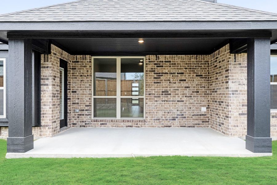 Covered back patio with brick walls, dark wood columns, concrete floor, and large window overlooking green lawn. Covered back patio with brick walls, dark wood columns, concrete floor, and large window overlooking green lawn.