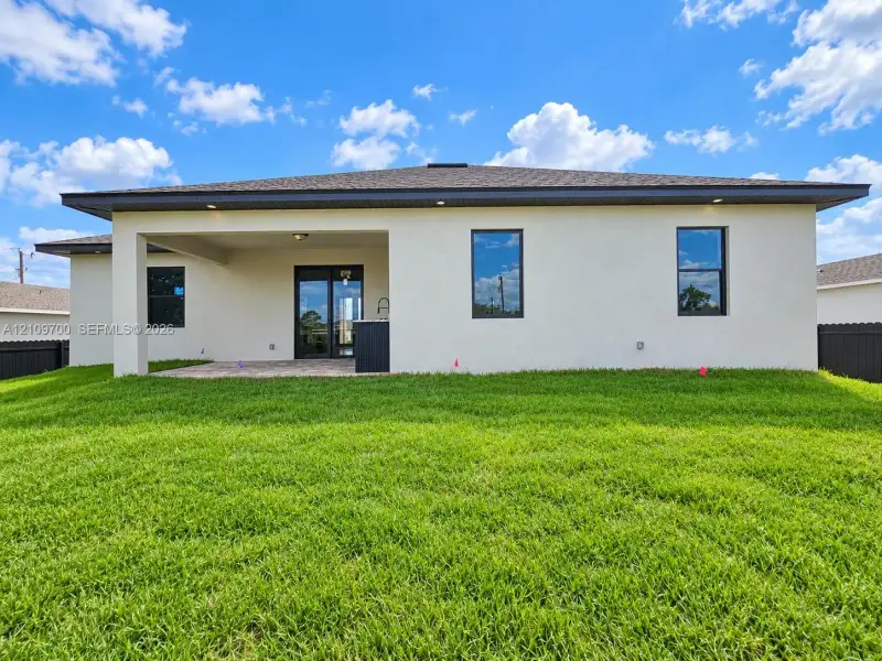 Stucco exterior featuring a covered patio, paved hardscaping, black-framed windows, and a built-in outdoor sink