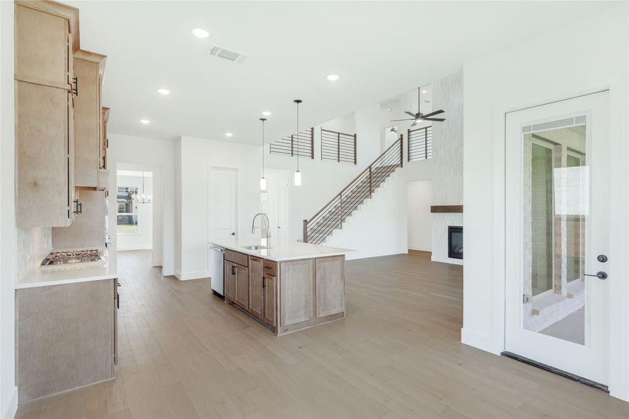 Open-concept kitchen with wood island, light hardwood floors, and staircase visible in background