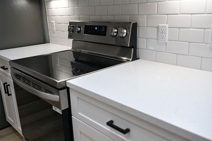 Kitchen featuring stainless steel electric stove, white cabinetry, and light stone countertops