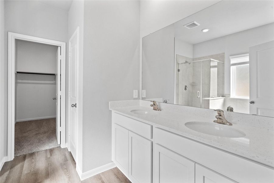 A bright and functional primary bath offering dual sinks for busy mornings, a large mirror, soaking tub, and a modern glass-enclosed shower, creating a serene and efficient space.